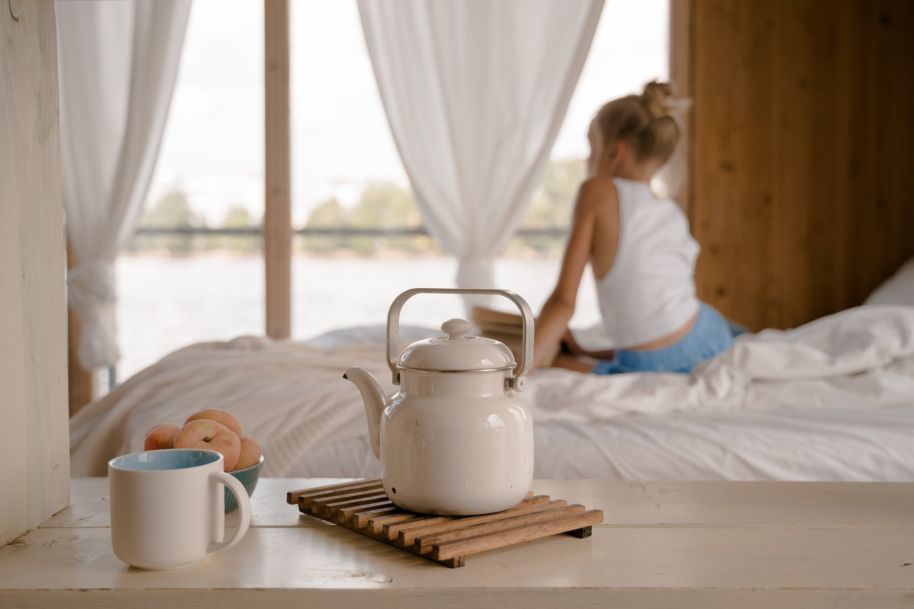 young girl sitting on bed with breakfast on table