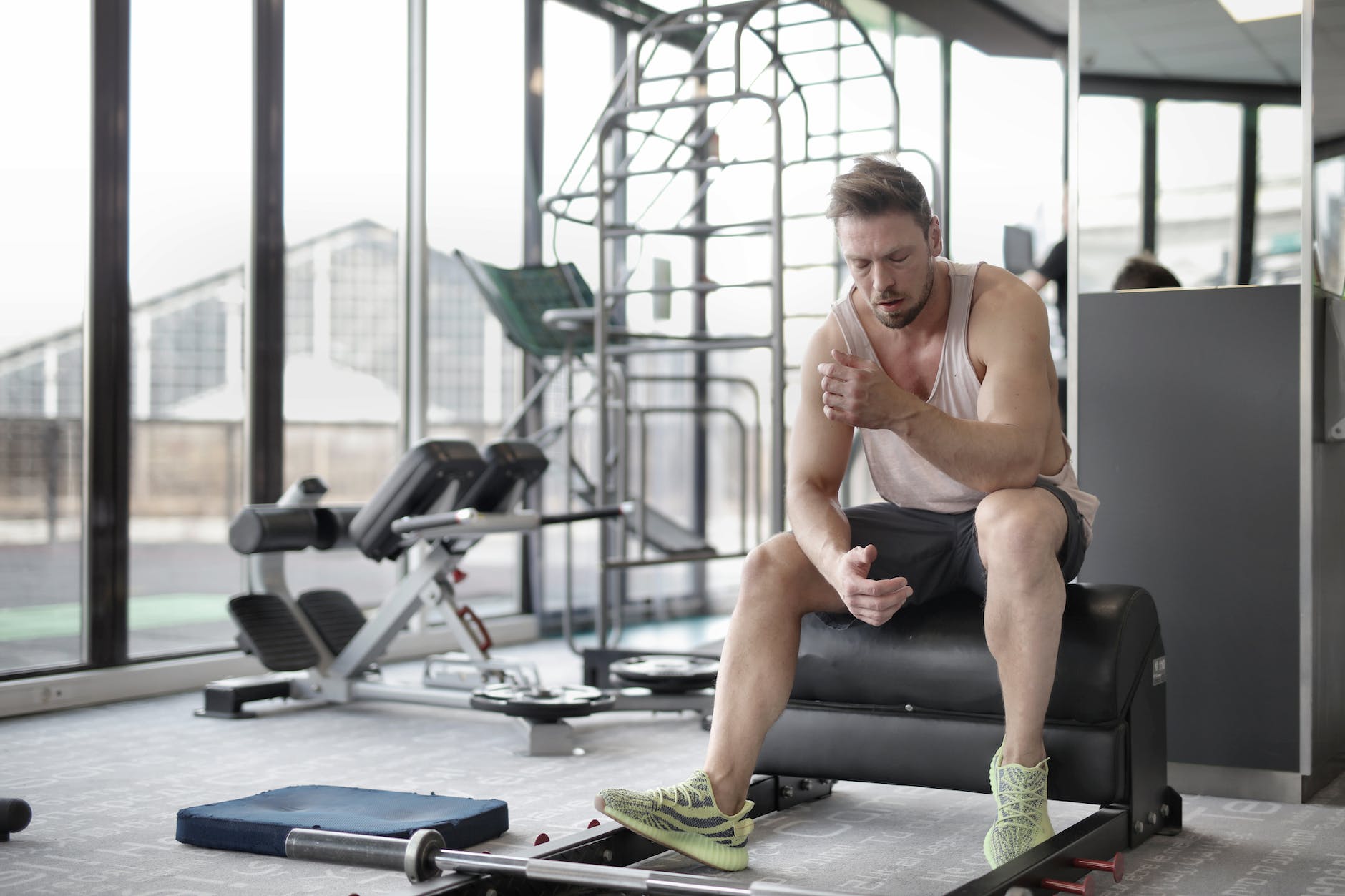 tired muscular male athlete resting after weightlifting workout in modern fitness center