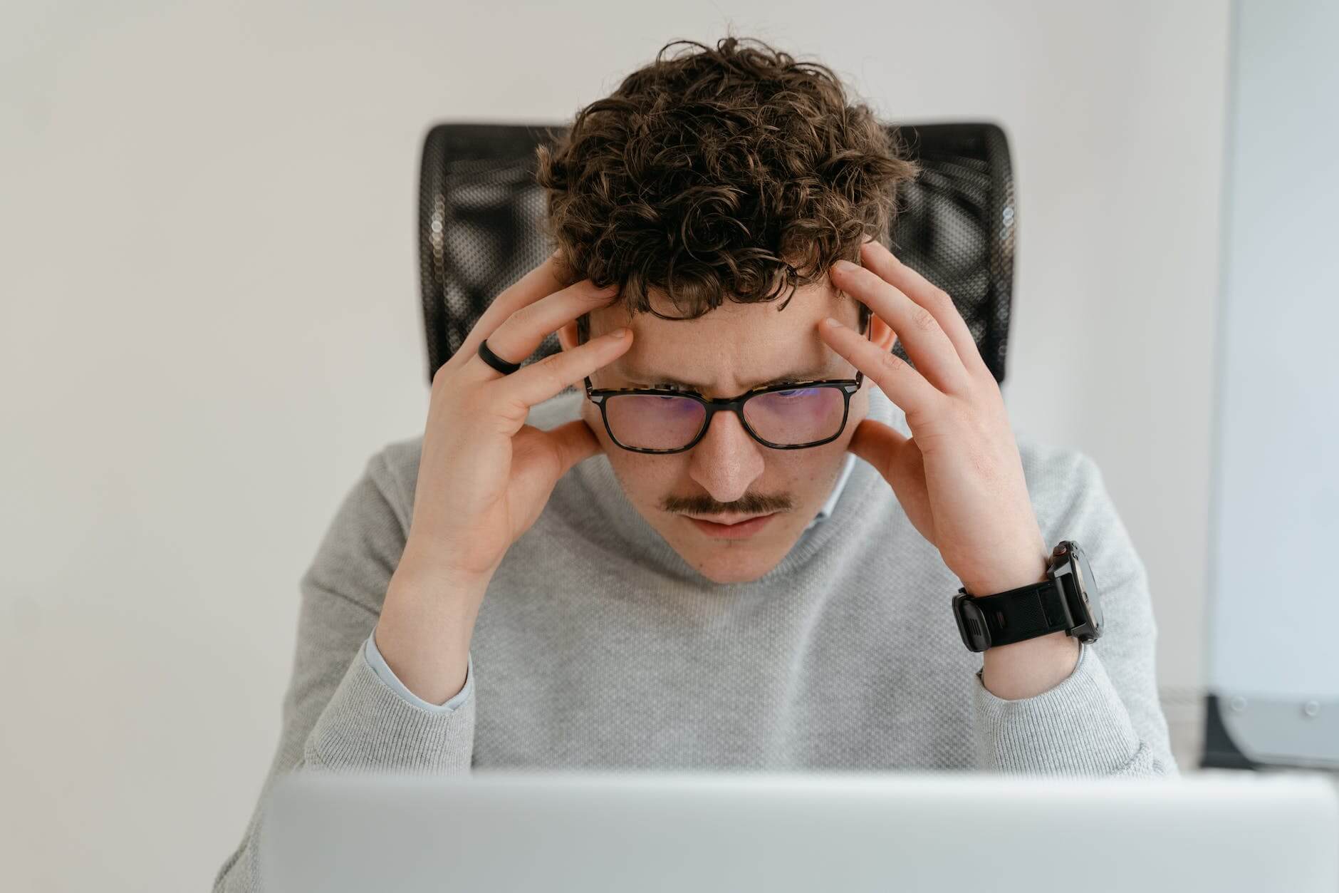 man in gray sweater holding his head with hands