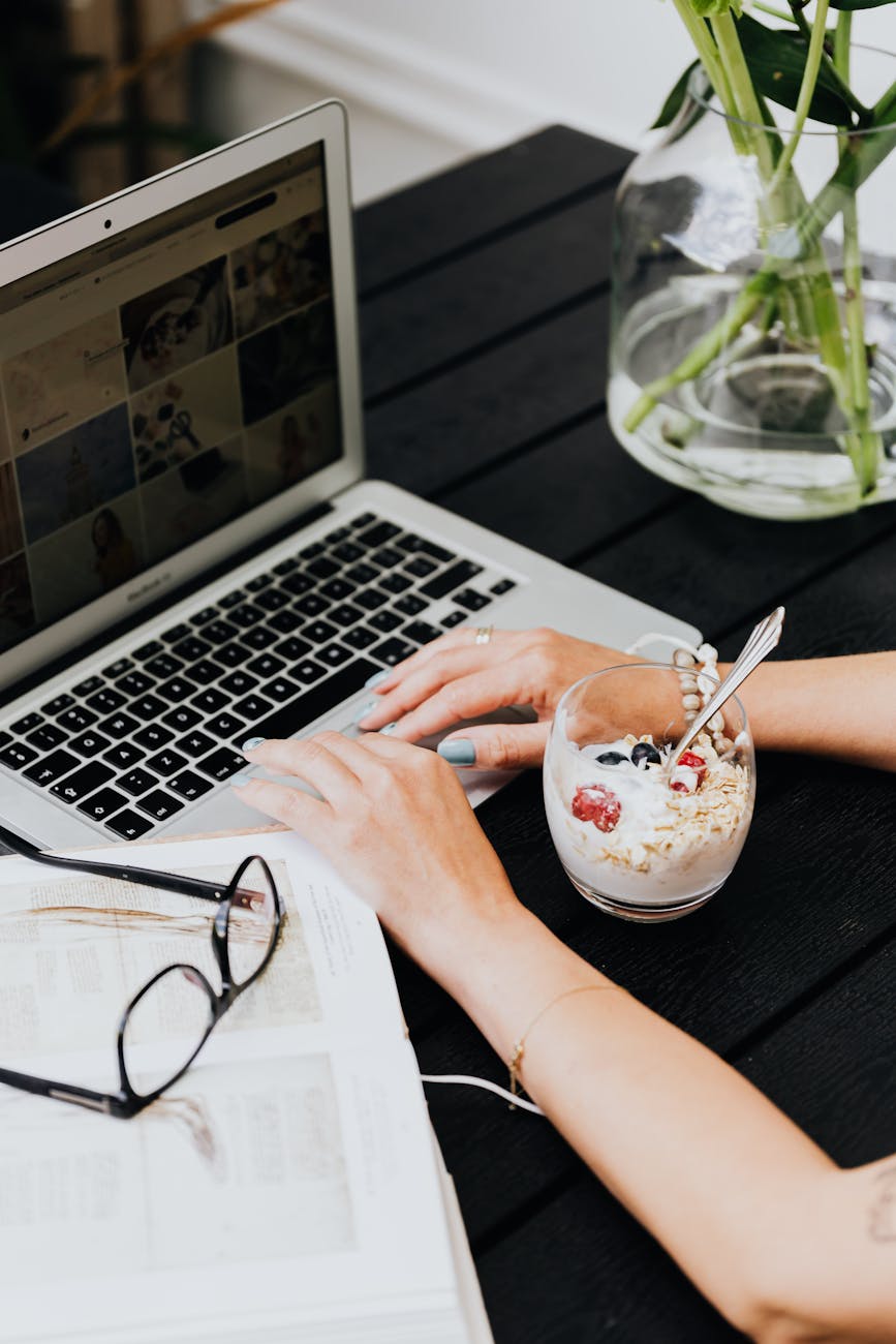 woman using a laptop at the table and eating yogurt with oats and fruit