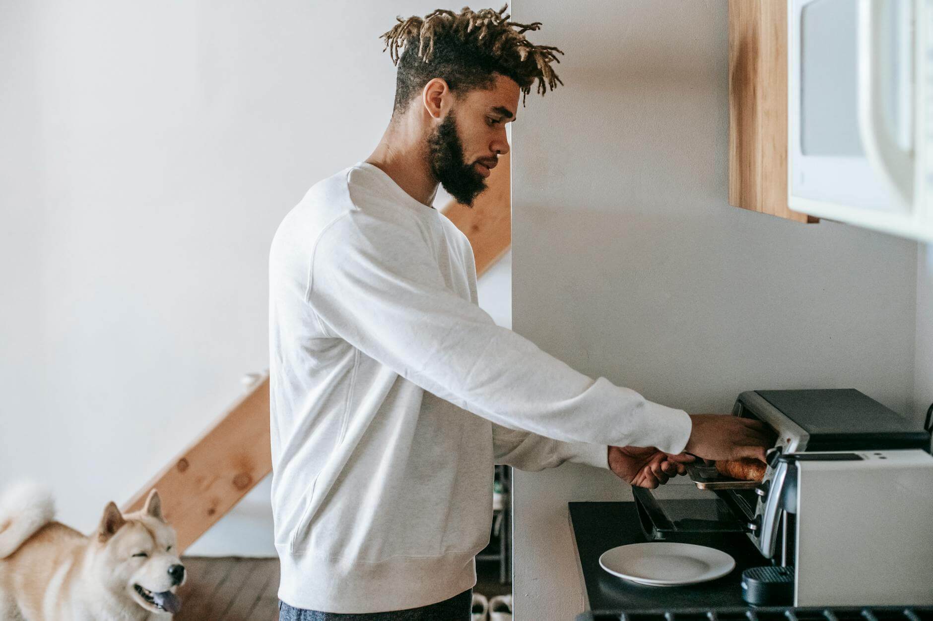 bearded young black man heating croissant in microwave oven standing near dog