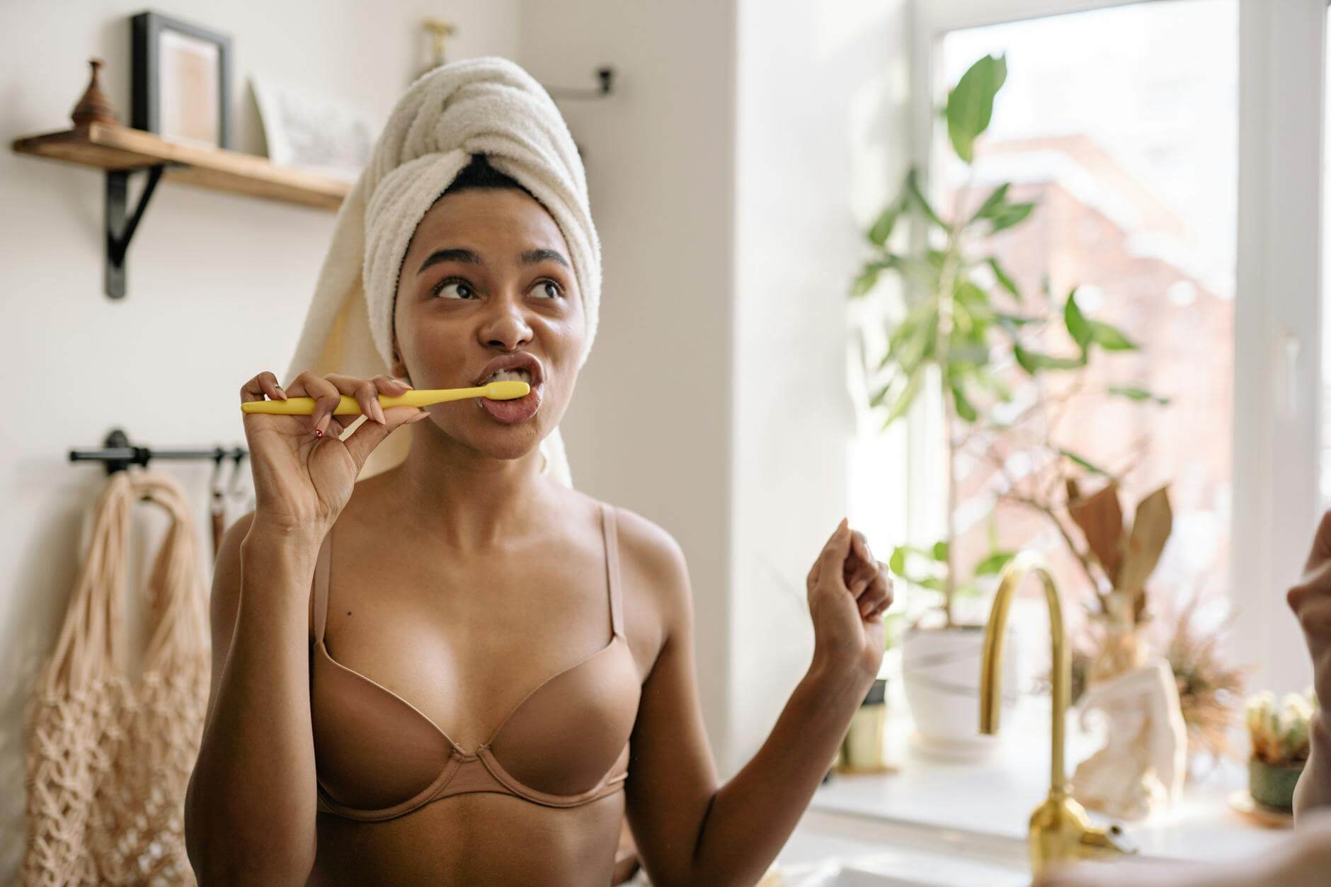 a woman in bra wearing a head towel brushing her teeth