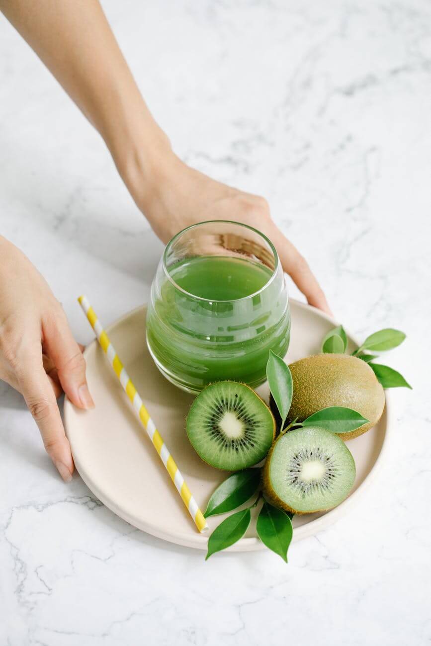 a person holding a plate with kiwi fruits and juice on a drinking glass