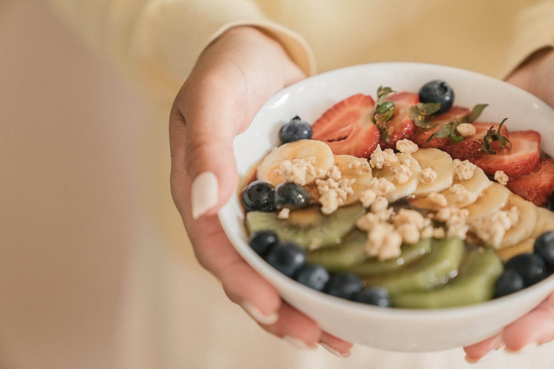 person holding white ceramic bowl with sliced fruits