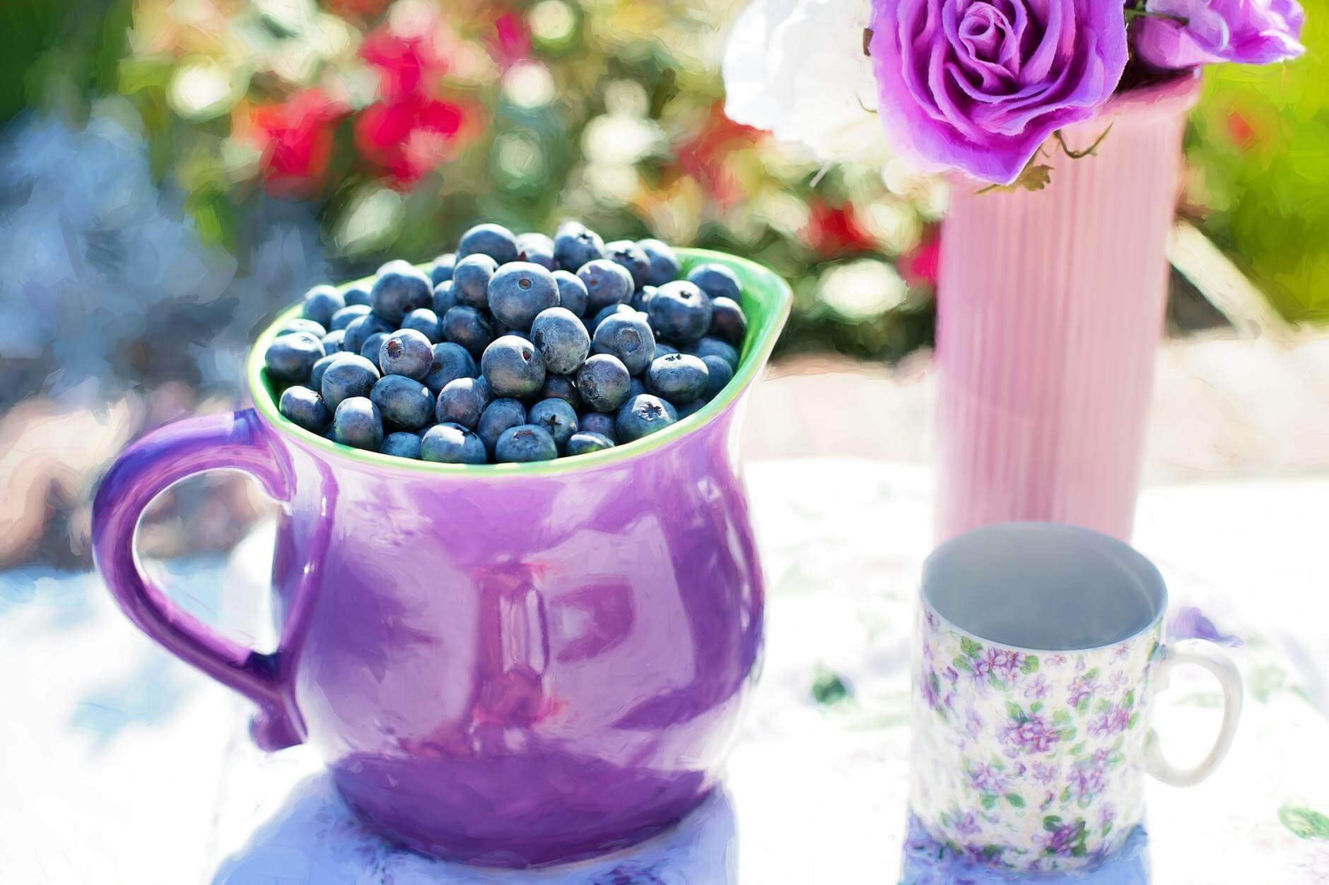 black berries on purple container beside white and purple floral mug