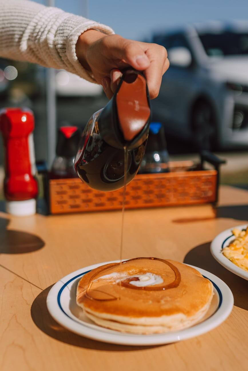 a person pouring syrup on pancakes